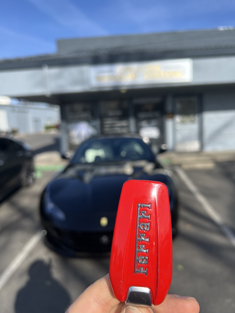 A red Ferrari key fob held in front of a black Ferrari car in Gold River, CA.