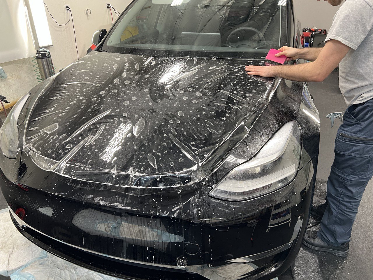 Technician applying paint protection film to the hood of a black Tesla using a squeegee in Gold River.