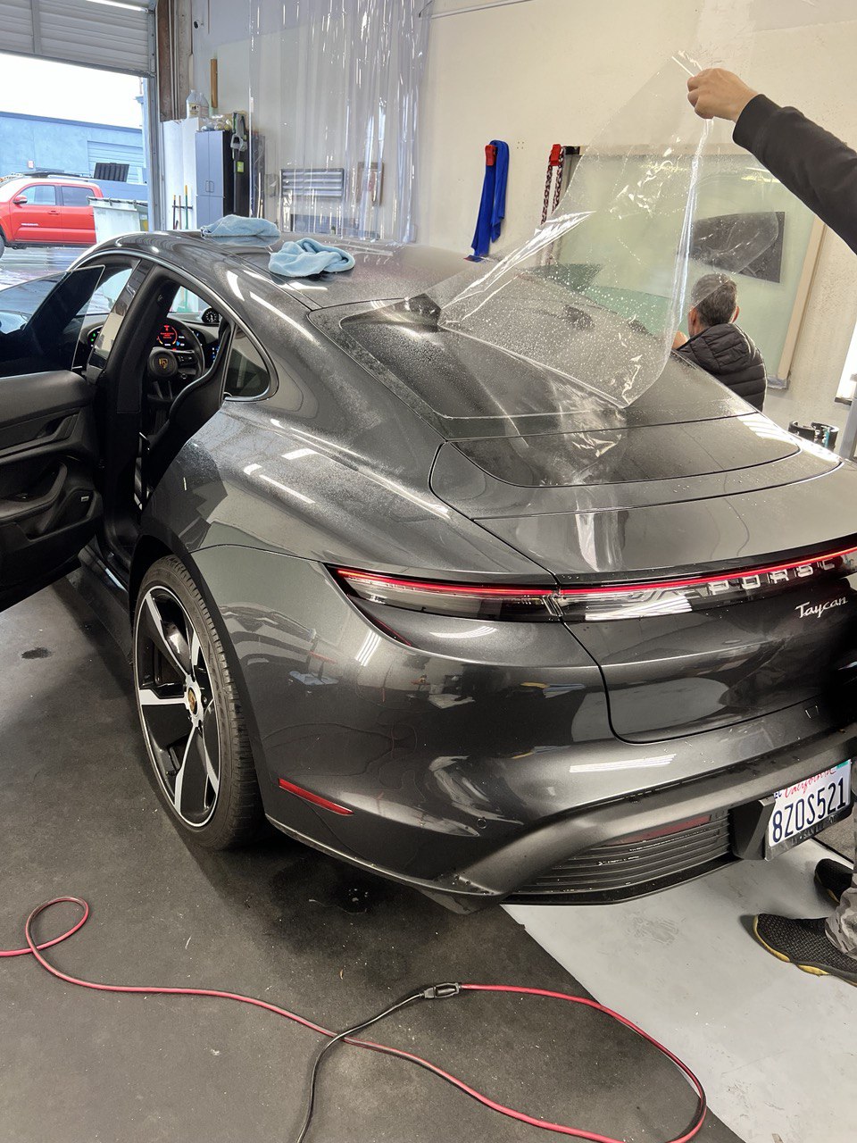 Technician applying clear paint protection film to the rear of a grey Porsche Taycan.