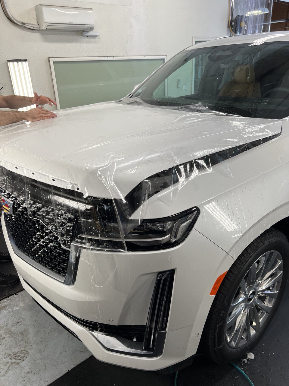Technician applying clear paint protection film to a white Cadillac Escalade hood.