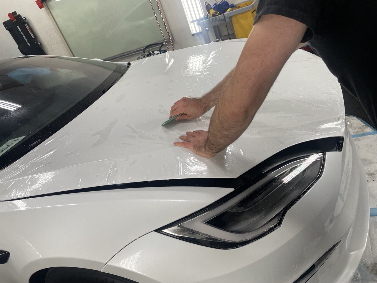 Technician applying clear paint protection film to a white car hood in Gold River, CA.